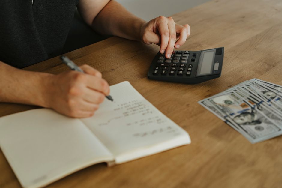 Unternehmerin plant an einem Holzschreibtisch mit Notizbuch und Taschenrechner das Budget für ein Projekt