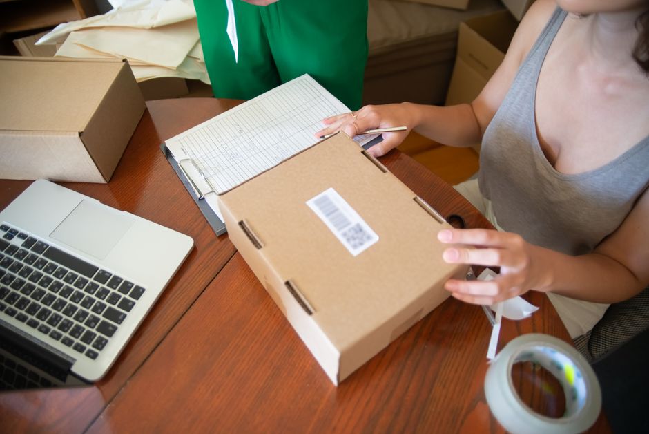 Inhaberin eines Onlineshops prüft Bestellungen auf dem Laptop, daneben gepackte Versandkartons auf dem Tisch