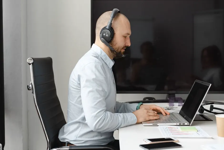 Ein Mann mit Kopfhörern arbeitet an einem Laptop und bedient ihn über die Tastatur.