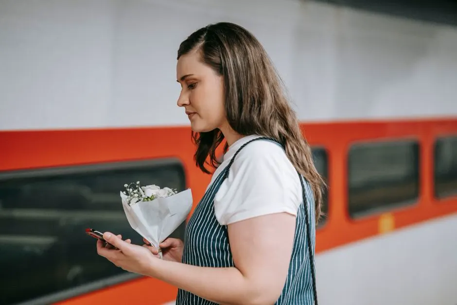 Frau hält ihr Smartphone in der Hand und wartet an einem Bahnsteig