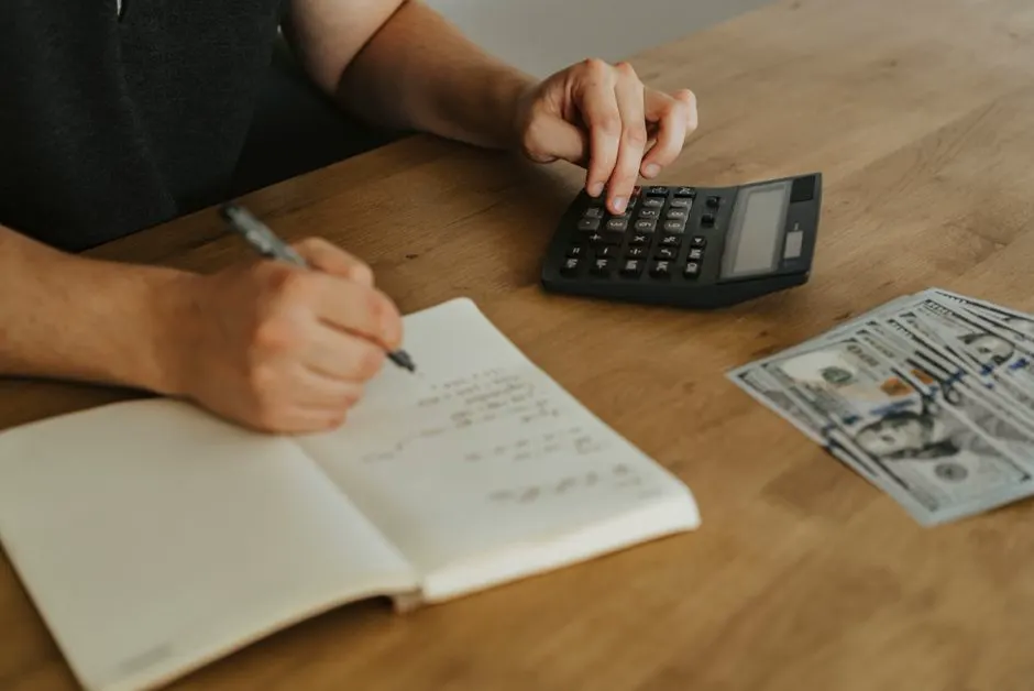 Unternehmerin plant an einem Holzschreibtisch mit Notizbuch und Taschenrechner das Budget für ein Projekt